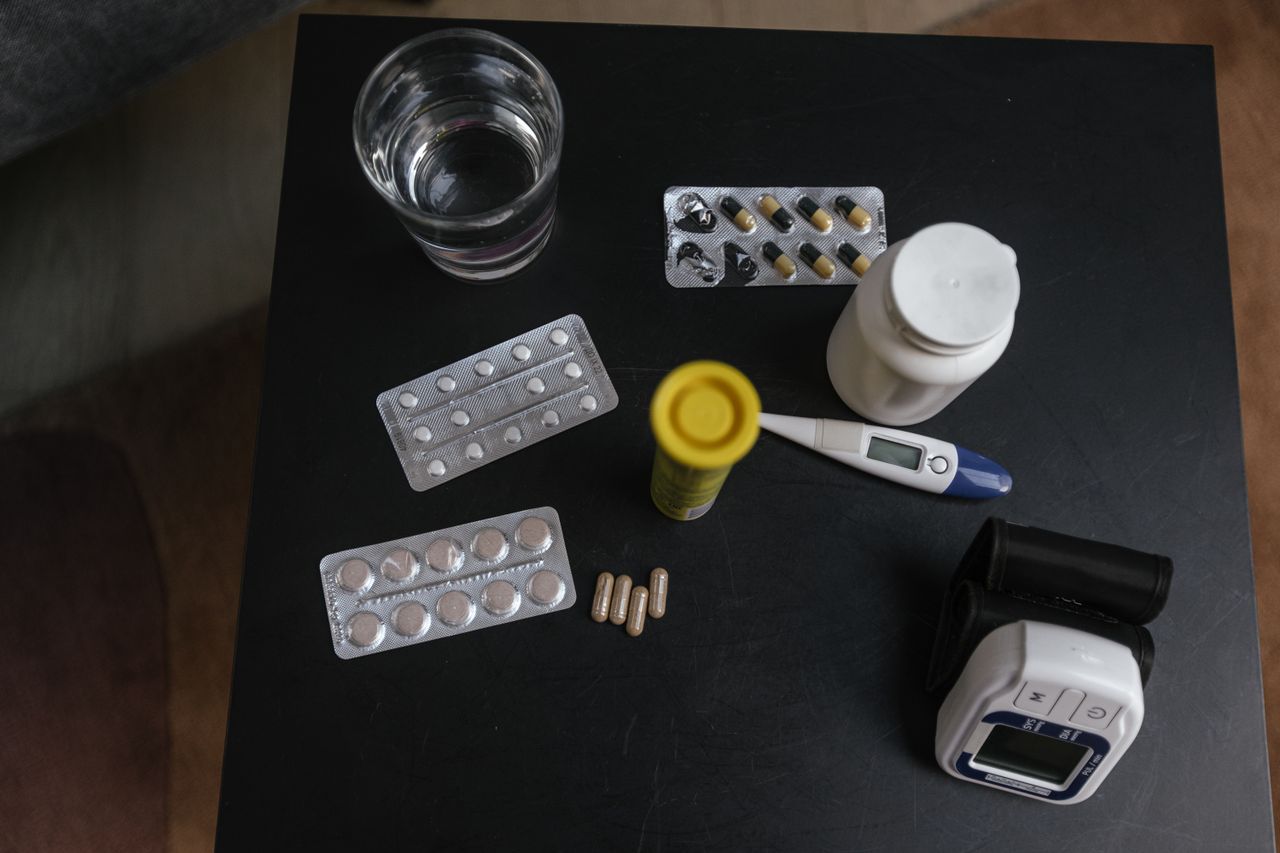Top view of various medications, tablets, and medical devices on a table with a glass of water.